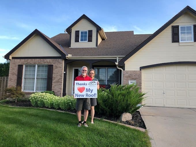 Couple holding an Innovative Roofing thank-you sign in front of their home with a newly installed roof
