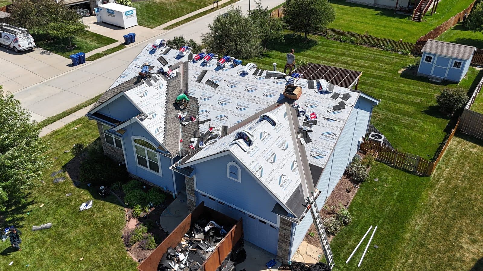 Aerial view of an Innovative Roofing crew installing shingles on a residential roof with branded underlayment