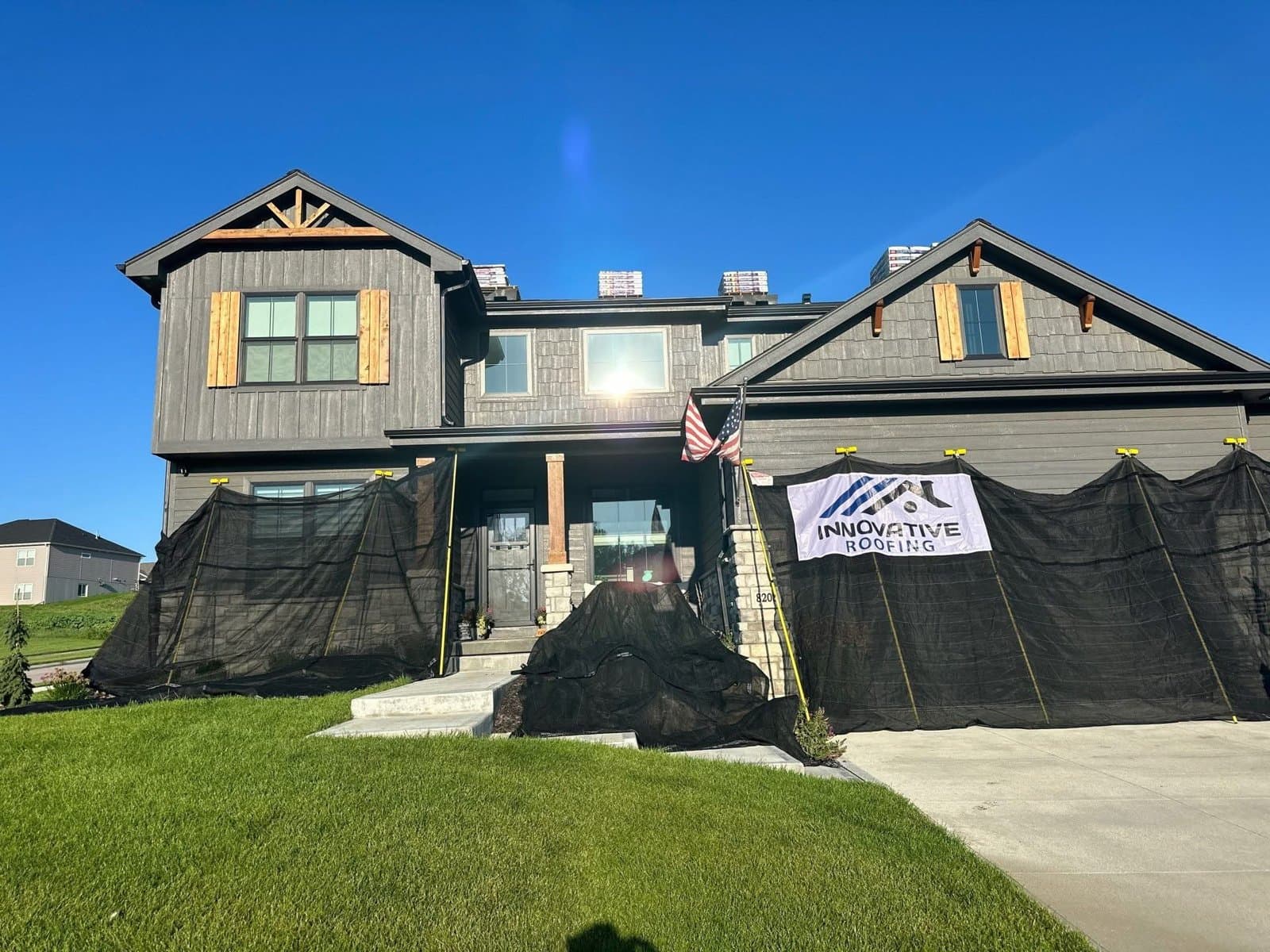 Two-story home with debris netting and new shingle bundles staged on the ridge