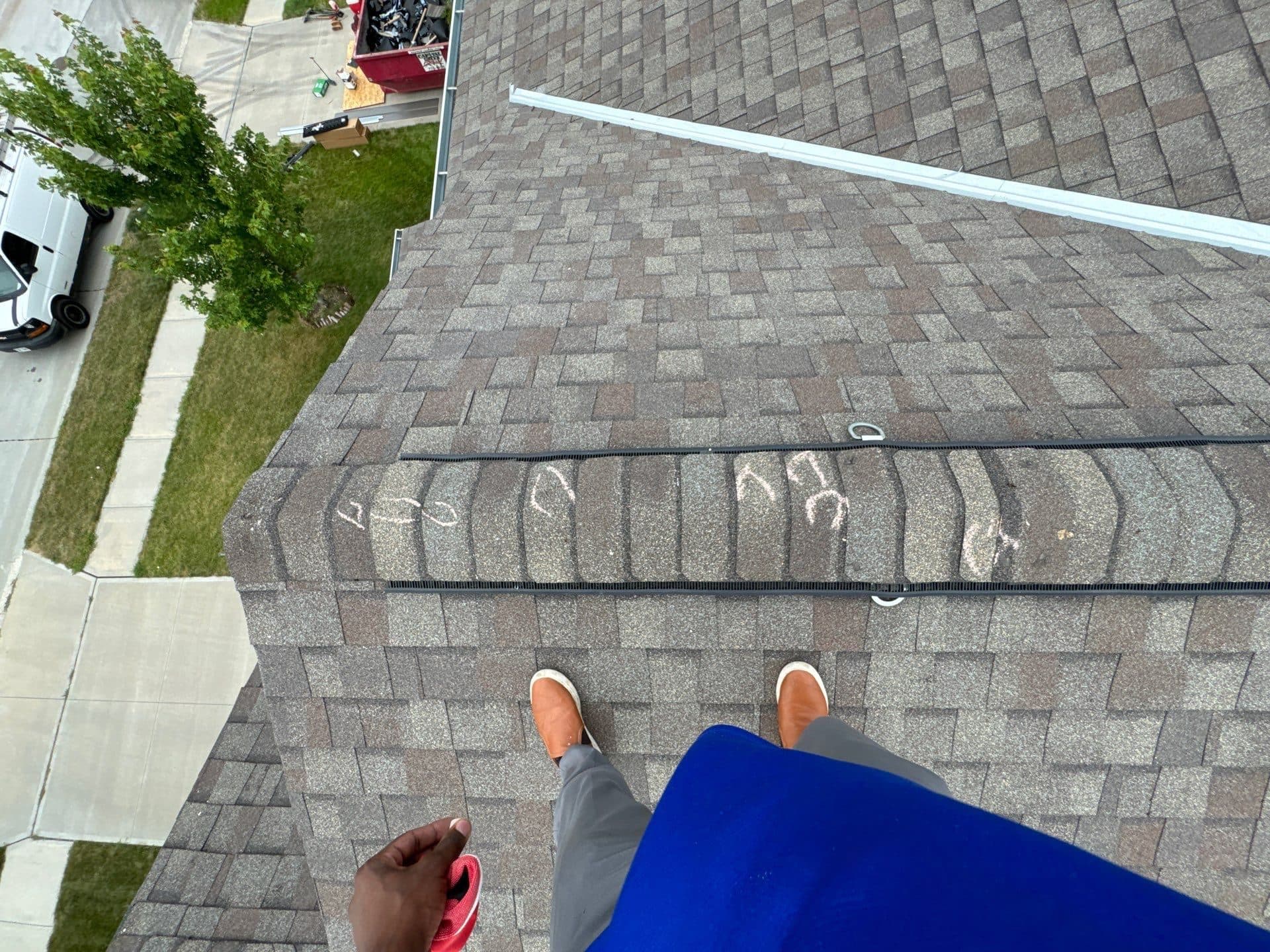 Roofer’s view along a shingle ridge with chalk marks and safety anchors during an active roofing job