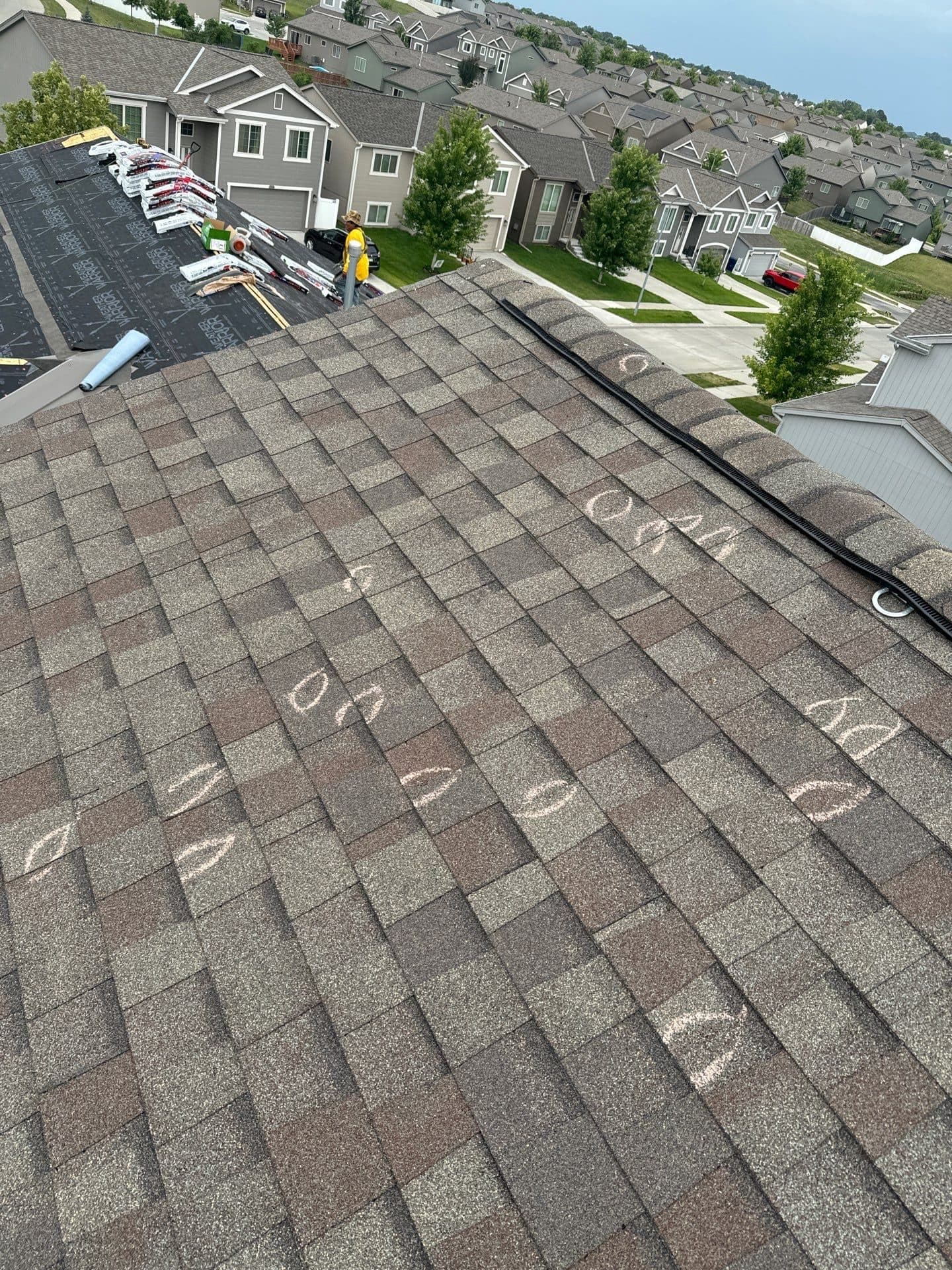 Roof with chalk-marked hail hits and new underlayment staged while a crew member works on a nearby section