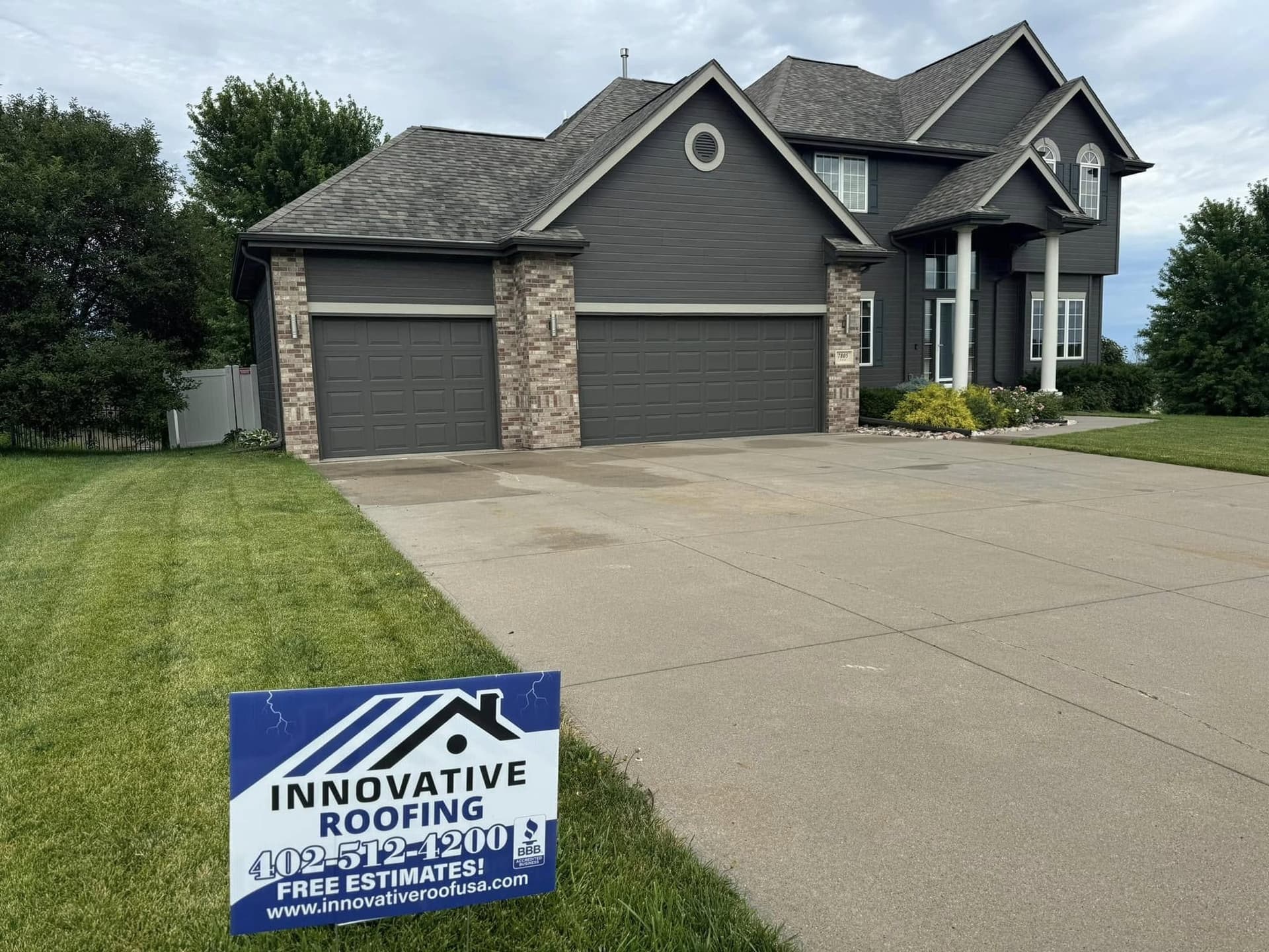 Large gray two-story home with a new dark shingle roof and an Innovative Roofing yard sign by the driveway