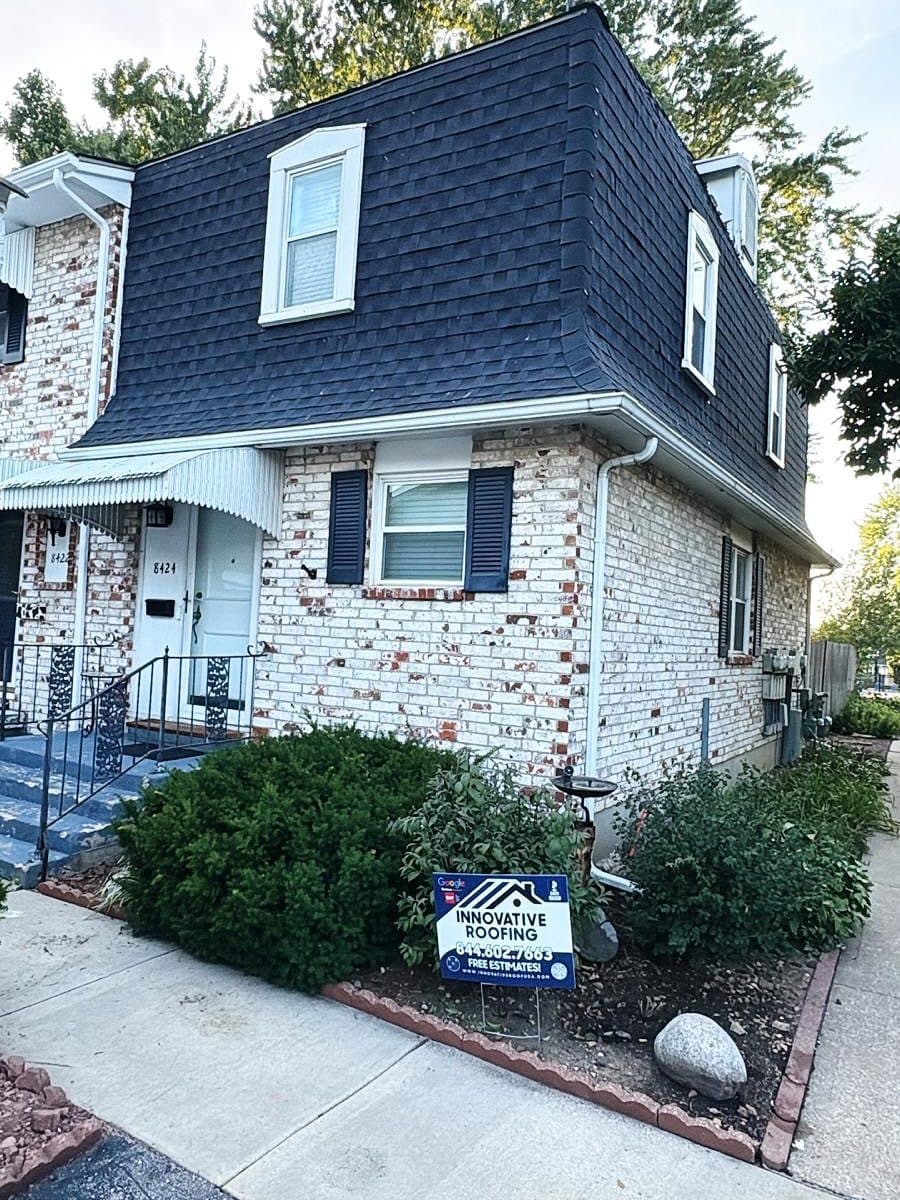 Brick townhome with a dark mansard roof and Innovative Roofing free-estimate yard sign in the landscaping