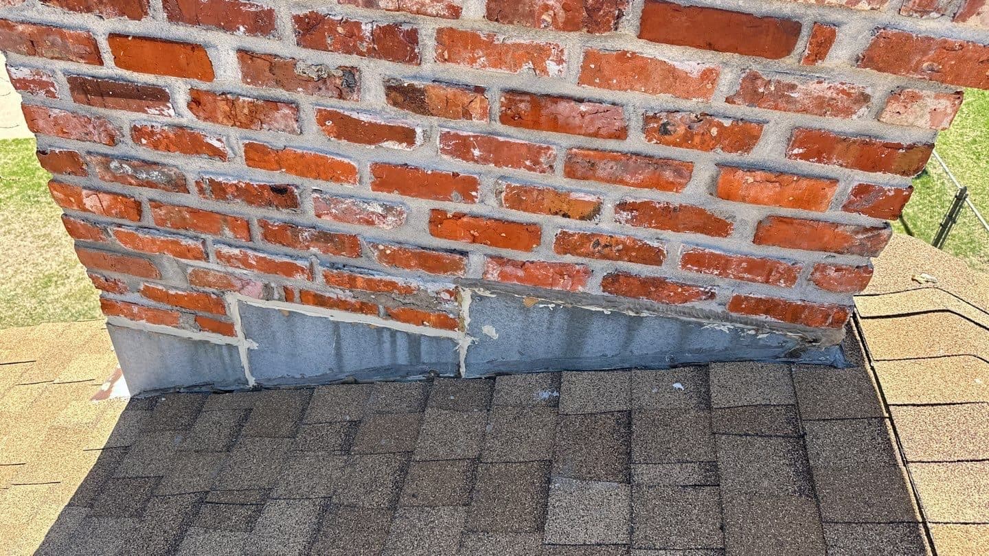 New metal flashing where a brick chimney meets a new gray shingle roof