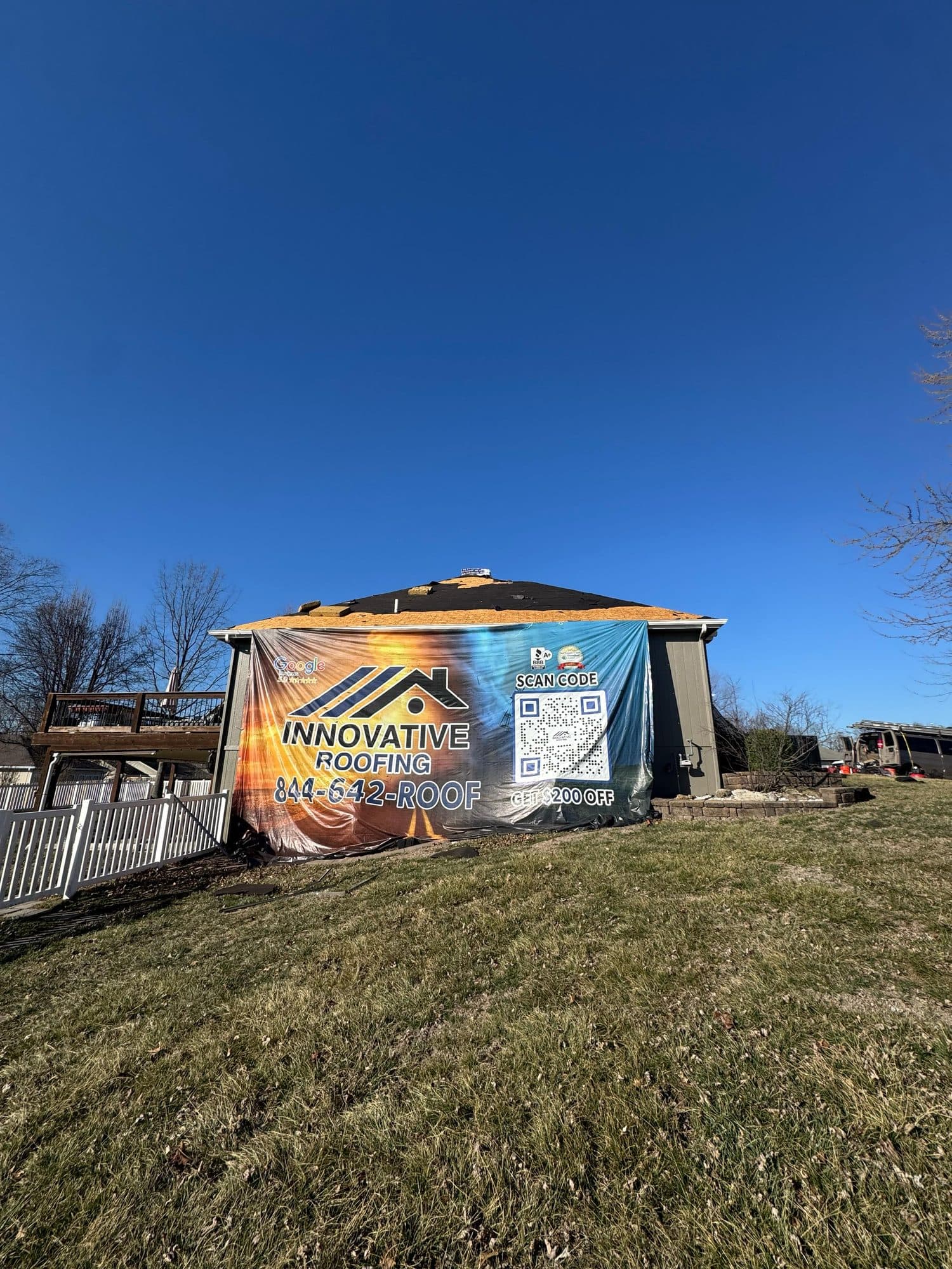 House with Innovative Roofing banner on the side wall while roof sheathing is exposed during replacement
