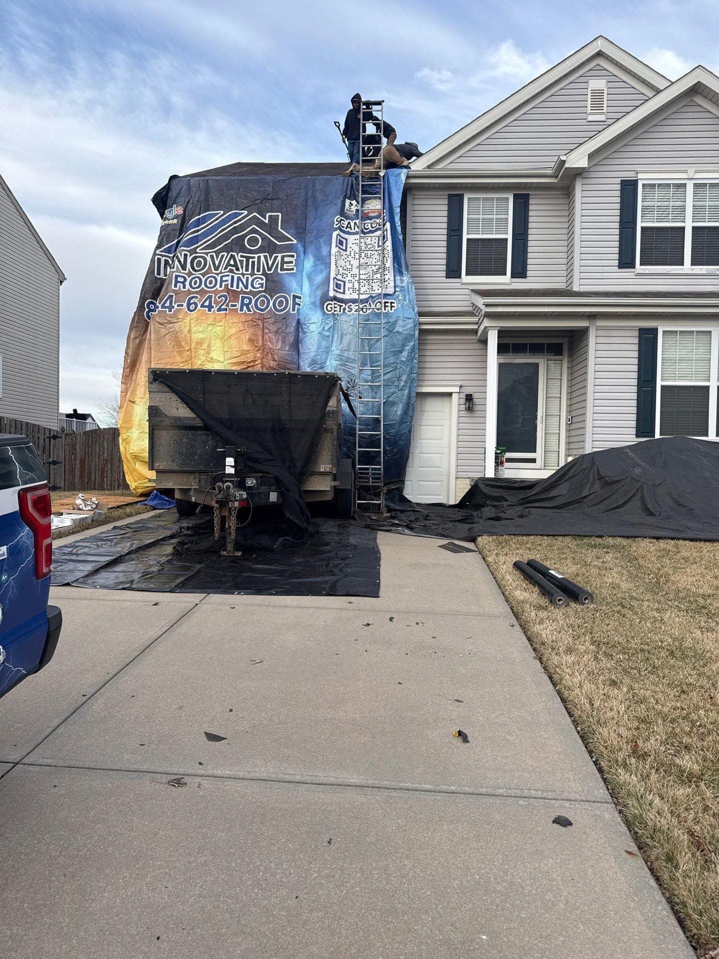 Residential roof replacement with Innovative Roofing branded debris tarp, ladder, and dump trailer protecting the driveway