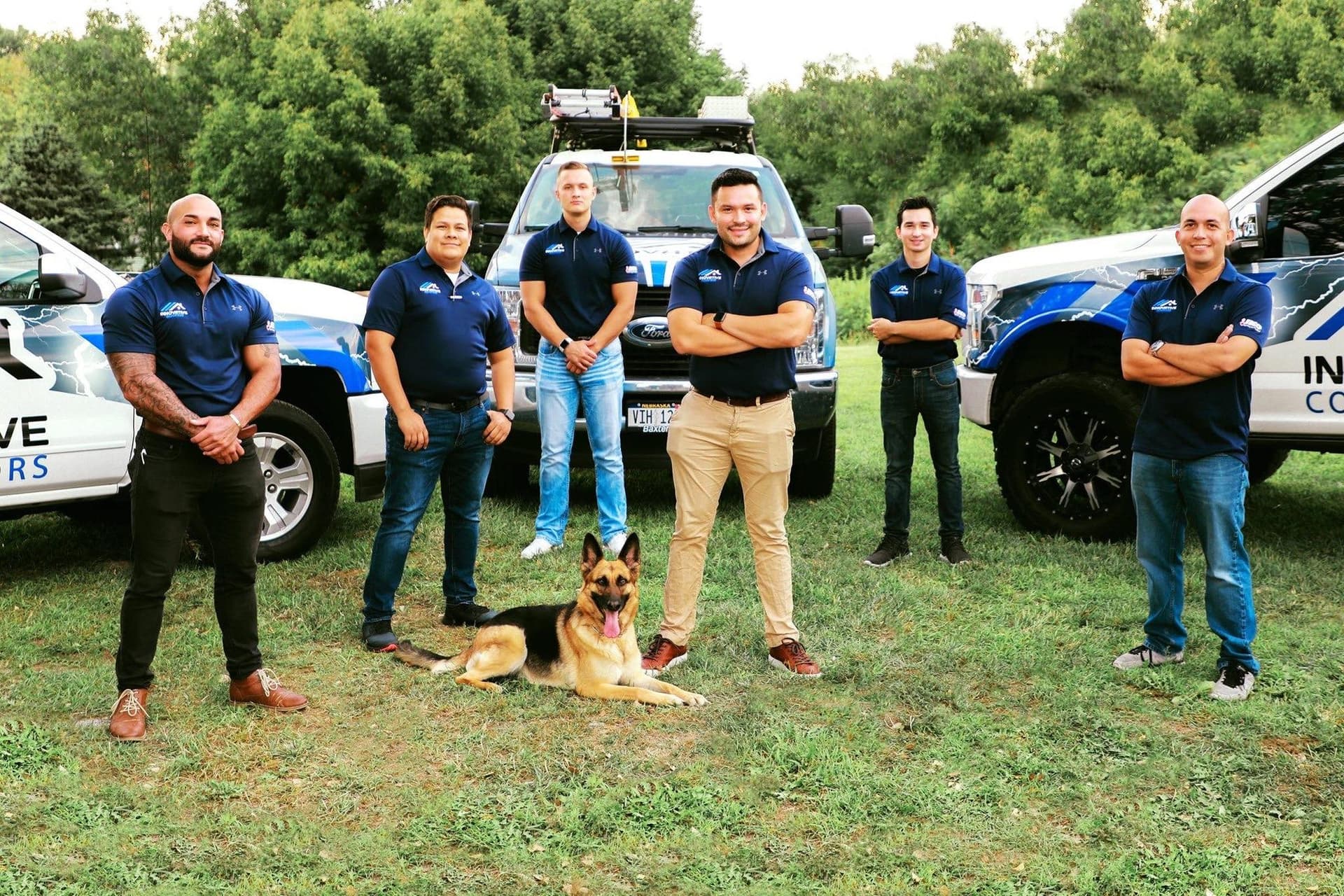 Innovative Roofing team in matching polos posing with branded white pickup trucks and the company dog