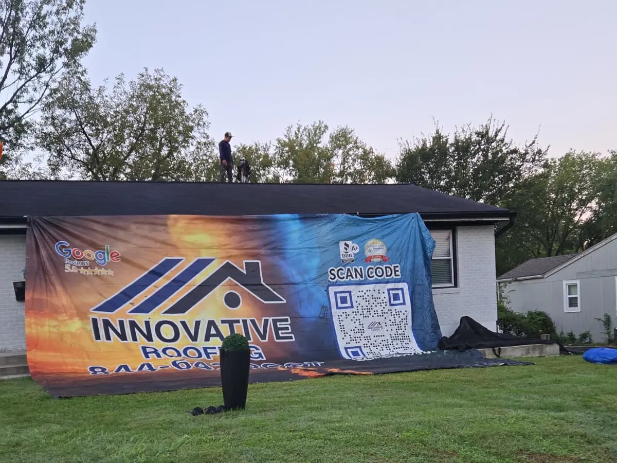Crew member on the roof of a single-story Kansas City area home behind a large Innovative Roofing job-site banner