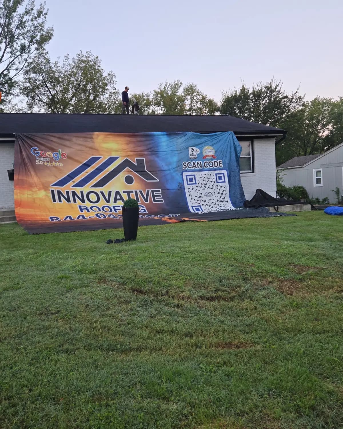 Crew member on the roof of a Kansas City area home behind an Innovative Roofing job-site banner