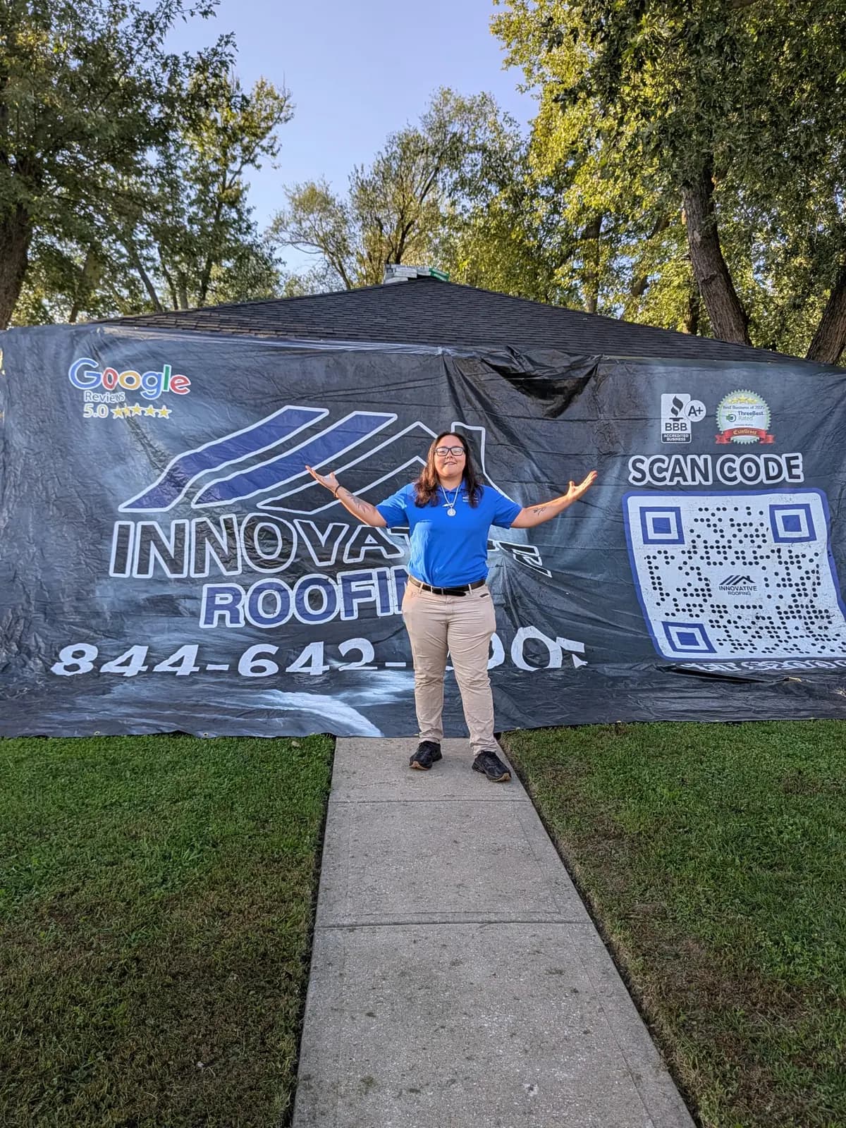 Innovative Roofing team member with arms open in front of the company job-site banner at a Kansas City area home