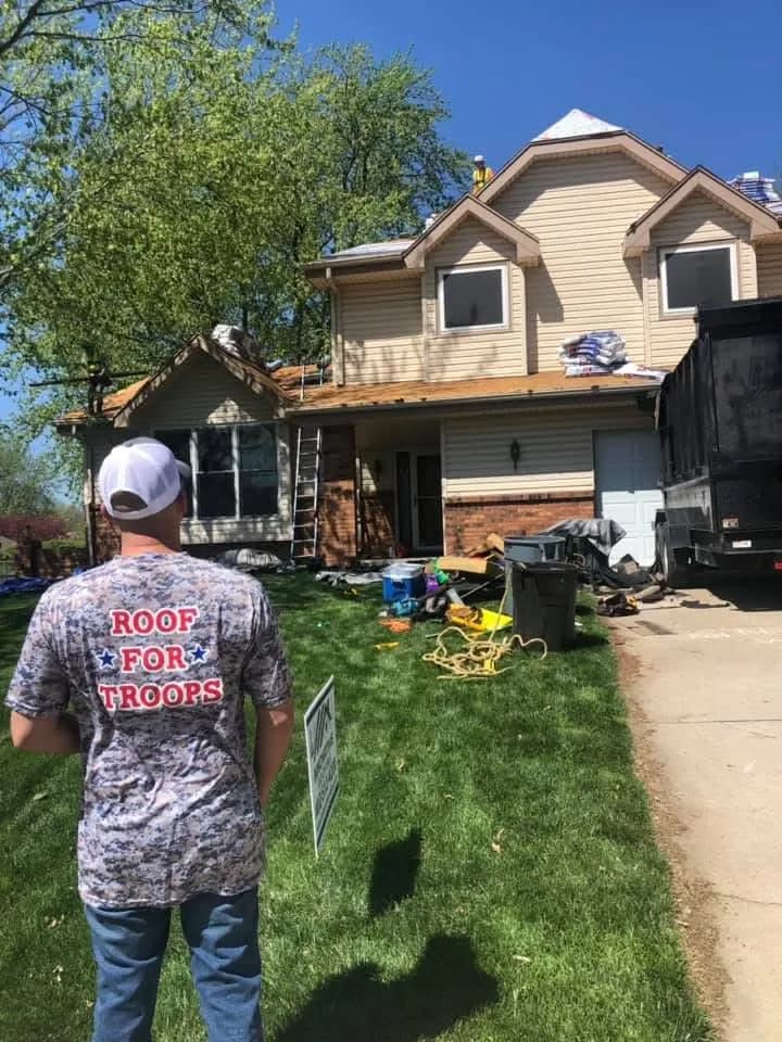 Two-story Kansas City area home during a roof replacement, with a ladder, materials on the roof and a dump trailer in the driveway