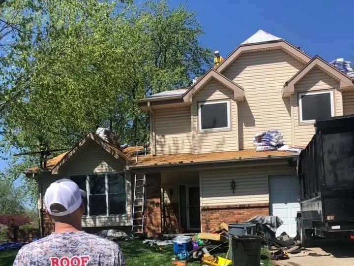 Two-story Kansas City area home during a roof replacement by Innovative Roofing, with a ladder and dump trailer on site